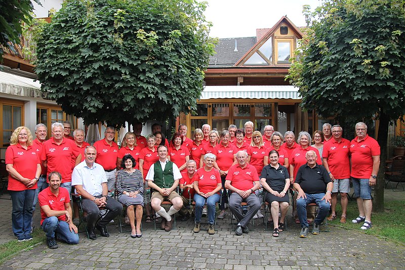 Die Teilnehmerinnen und Teilnehmer der Sportwoche haben sich für ein Gruppenfoto im Innenhof eines Lokals versammelt. Sie tragen beinahe ausschließlich rote Shirts. 