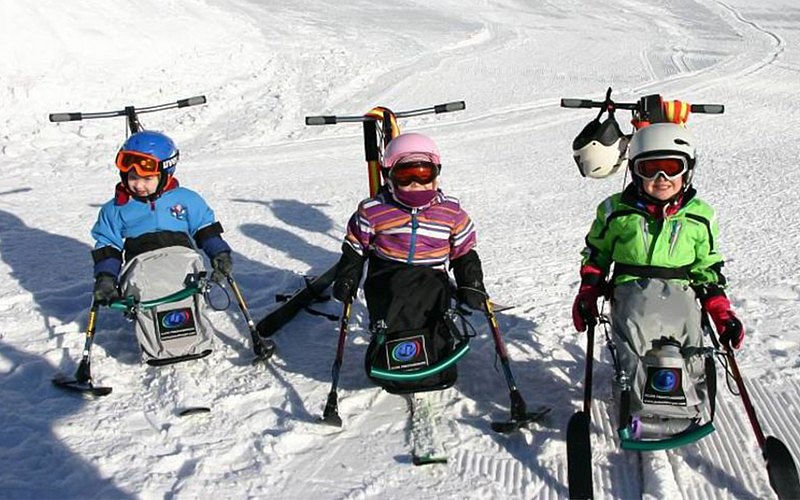 Drei Kids sitzen im Ski-Bob und lächeln in die Kamera. 