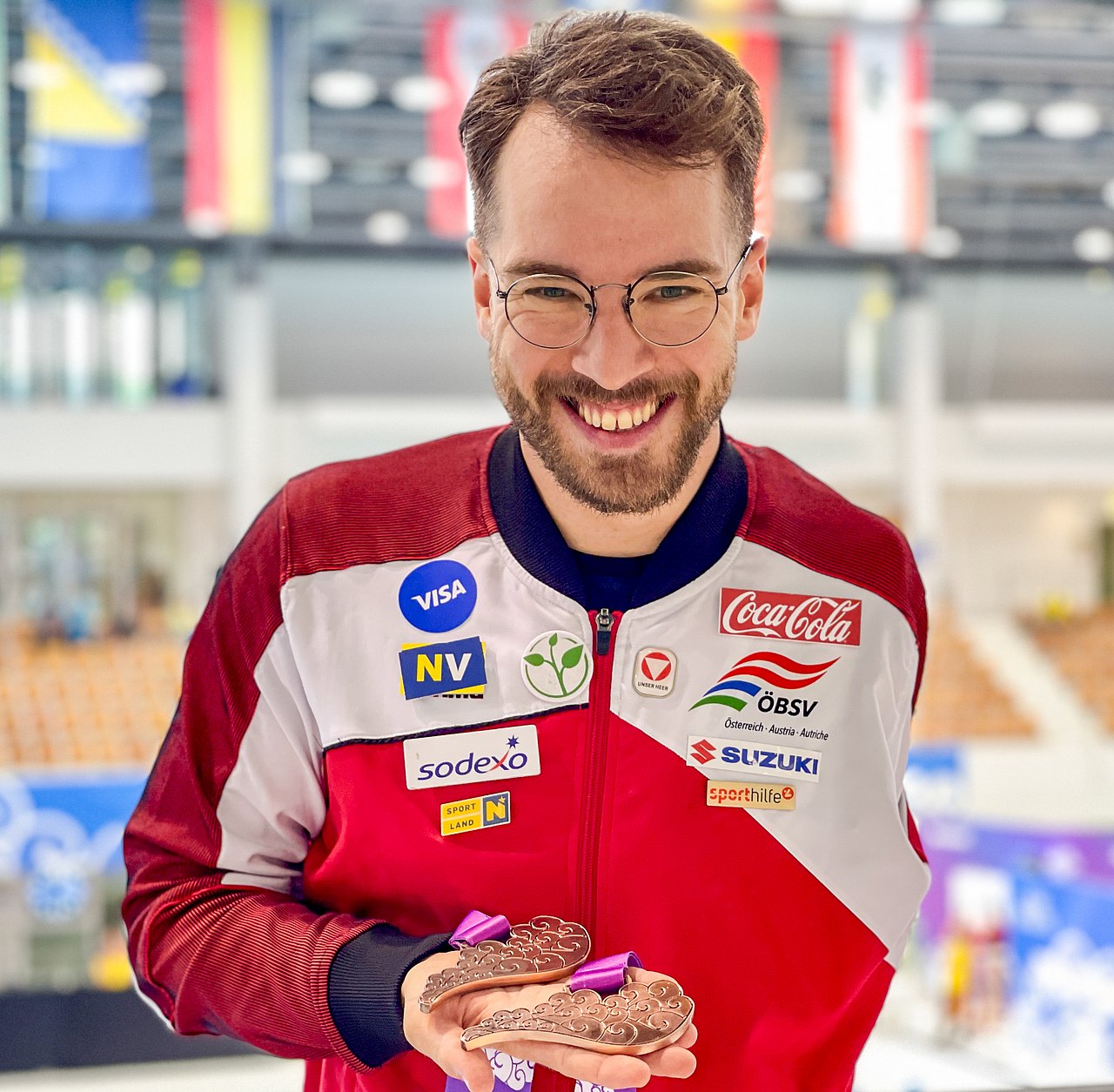 [Translate to Deutsch (Leichte Sprache):] Der Schwimmer Andreas Onea hält die rechte Hand geöffnet, darin liegen zwei Bronzemedaillen. 