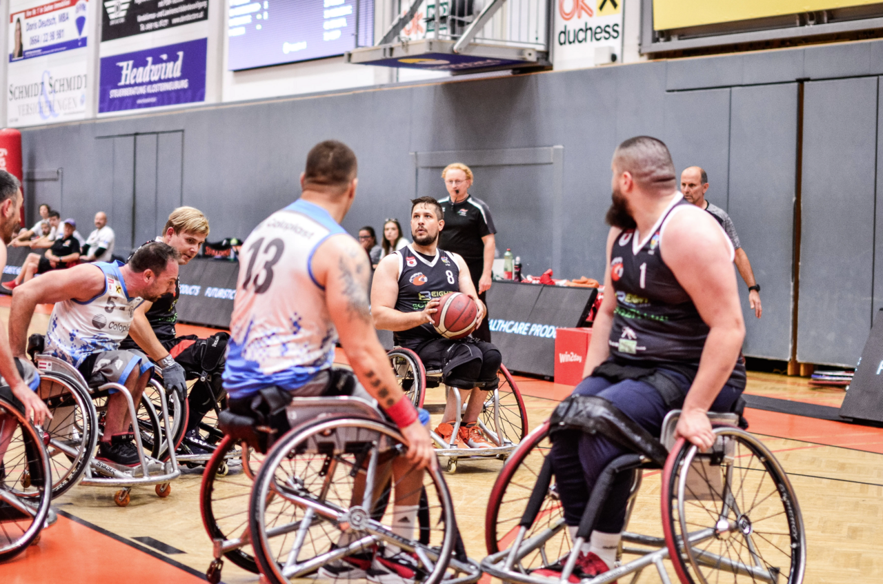 Der Rollstuhl-Basketballer Christoph Edler setzt im Spiel gegen die Sitting Bulls zum Wurf an. Er hat ein schwarzes Trikot an, die Bulls spielen in weiß. 