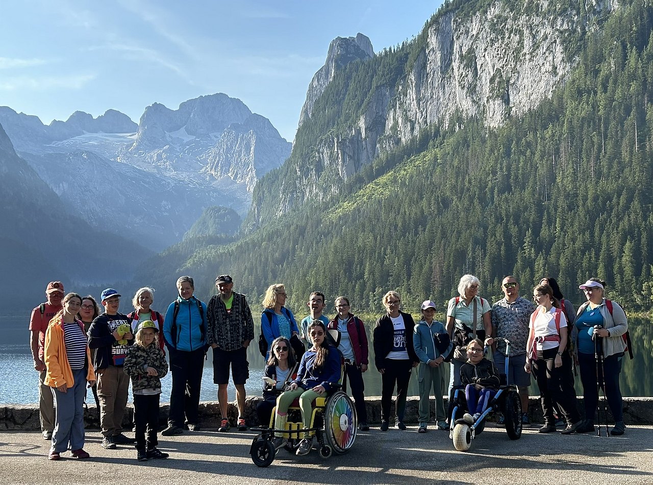 [Translate to Deutsch (Leichte Sprache):] Die Teilnehmenden der Sportwoche posieren für ein Gruppenfoto vor dem Hallstättersee. Dahinter scheint die Sonne zwischen den Bergen ins Tal.