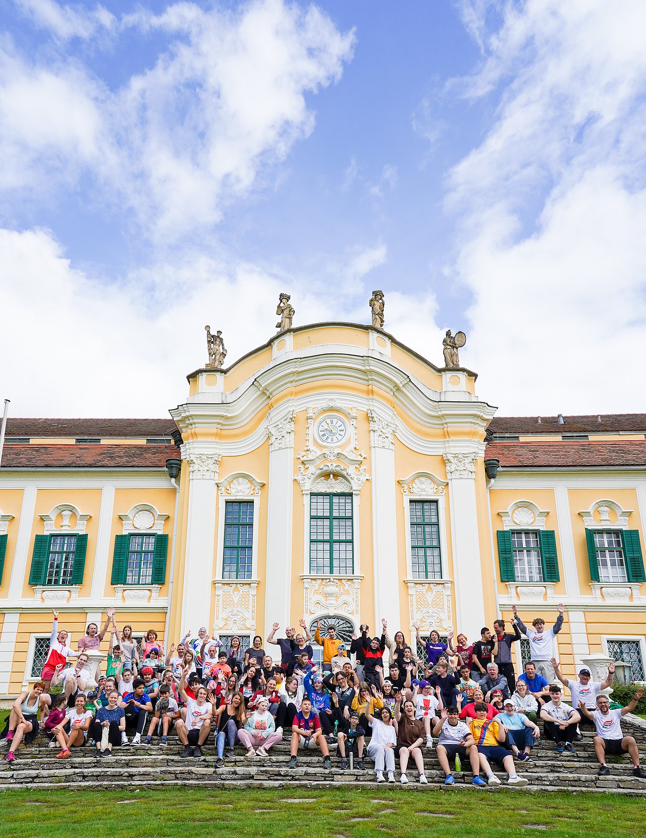 Die Teilnehmerinnen und Teilnehmer der Schulsportwoche sitzen und auf den Stufen vor dem Schloss Schielleiten und werfen freudig die Hände in die Höhe