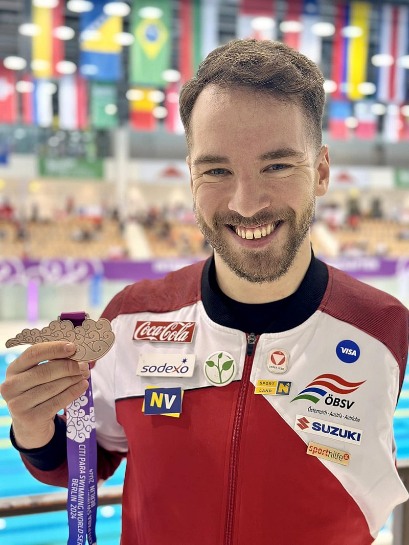 Andreas Onea lacht in die Kamera und hält seine bronzene Medaille in die Höhe. 