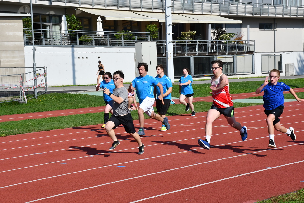 [Translate to Deutsch (Leichte Sprache):] 7 Sportler mit Downsyndrom sprinten auf der roten Laufbahn. 