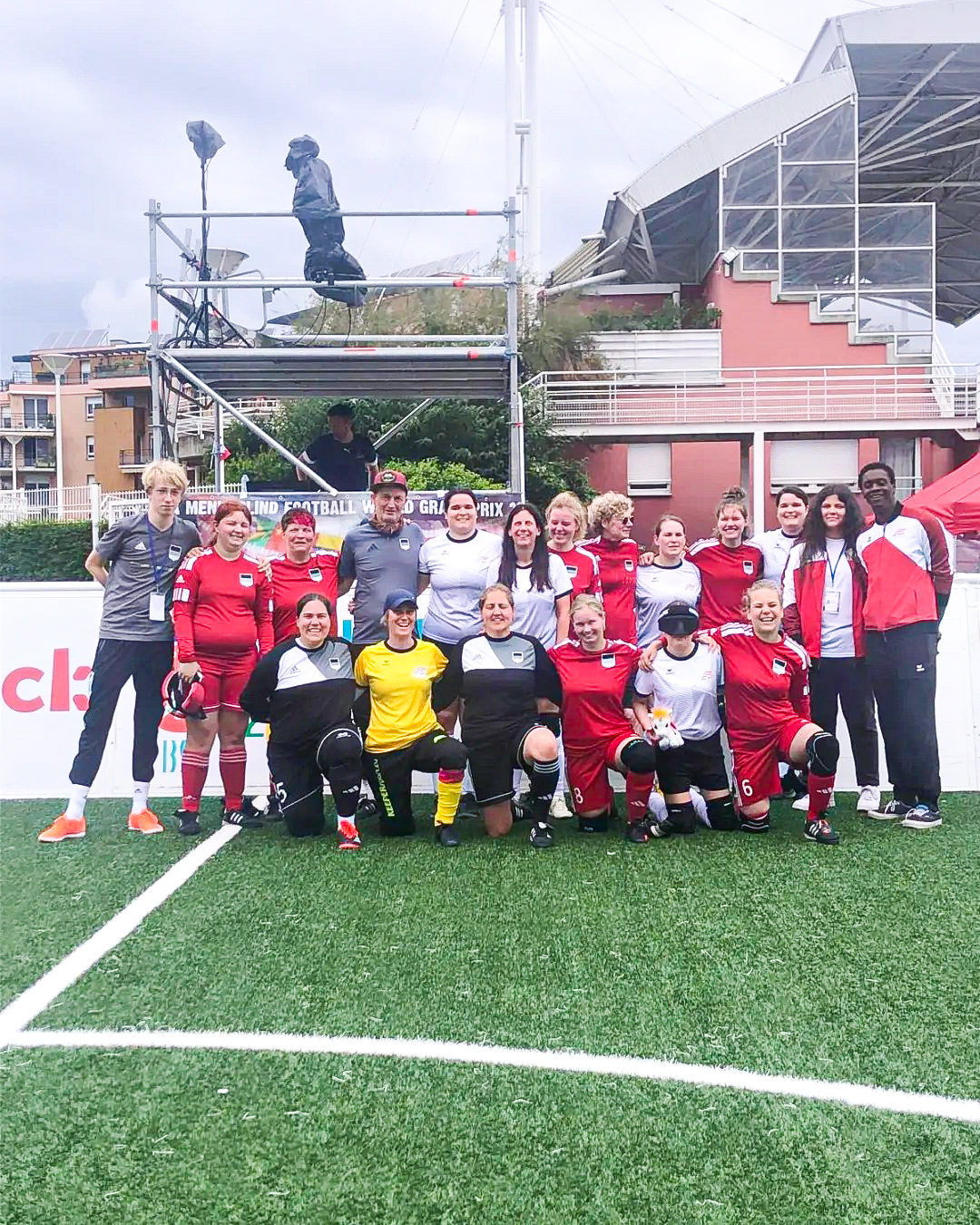 Das Bild zeigt die Blinden-Fußball-Damen-Nationalteams Österreichs und Deutschlands auf einem gemeinschaftlichen Gruppenfoto. Sie stehen auf dem Kunstrasen-Spielfeld vor der Bande und blicken in die Kamera. 